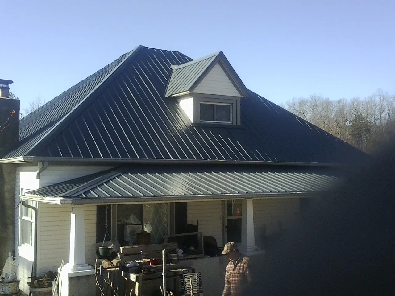 Dark blue standing seam metal roof with a dormer above a front porch in Harrison