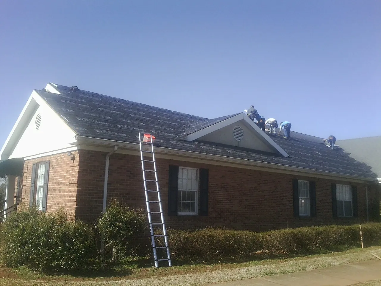 Crew tearing shingles off a brick ranch roof with a ladder set — Metal Roof Repair work by our crew in Harrison