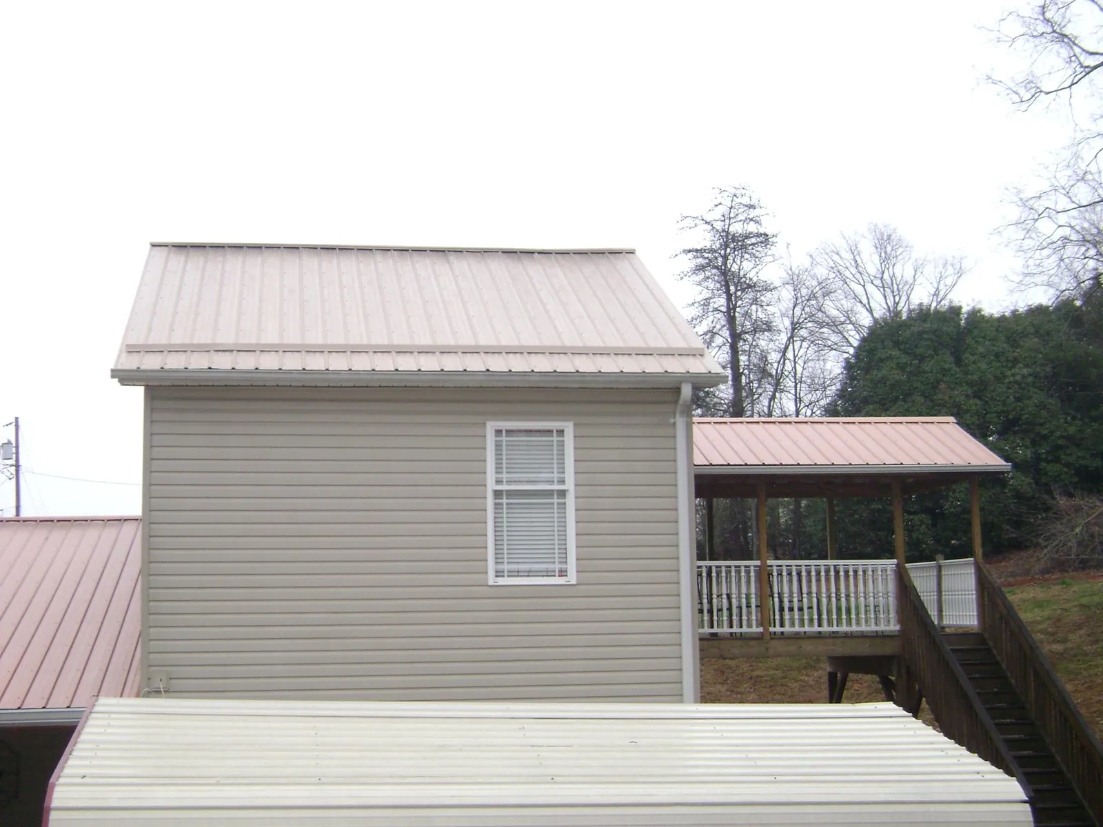Tan metal roofs on a two story addition and attached porch, from a Roof Replacement job in Harrison